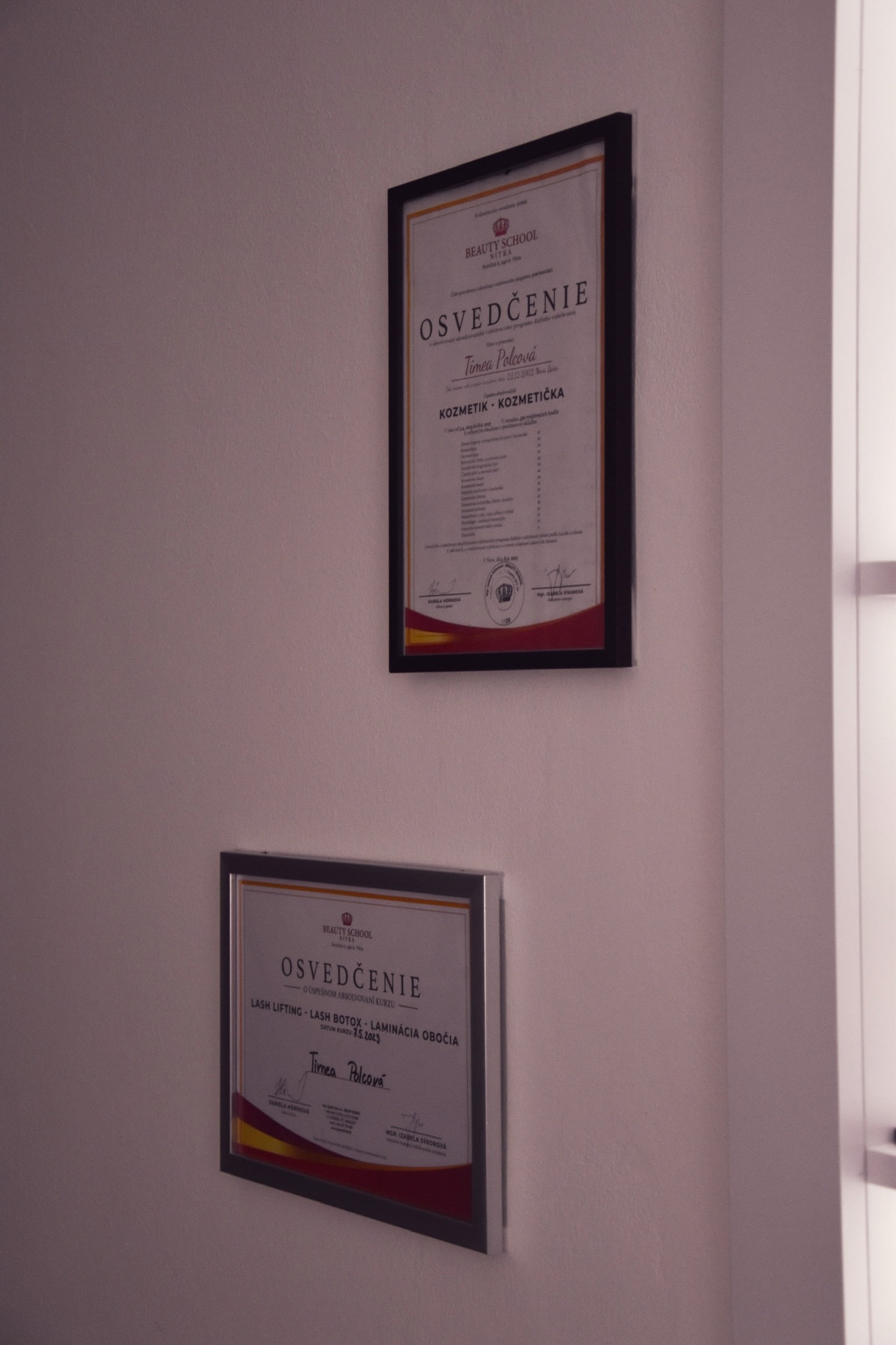 Profesionálne certifikáty Timey Polcovej zavesené na stene salónu